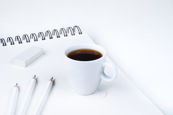 A cup of coffee with a spiral bound notebook, pens, and eraser.