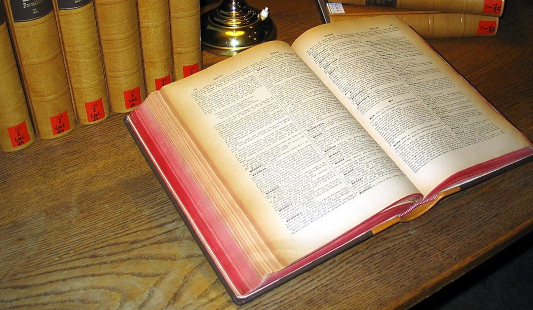 A Latin Dictionary open on a desk with other books and candle holder.