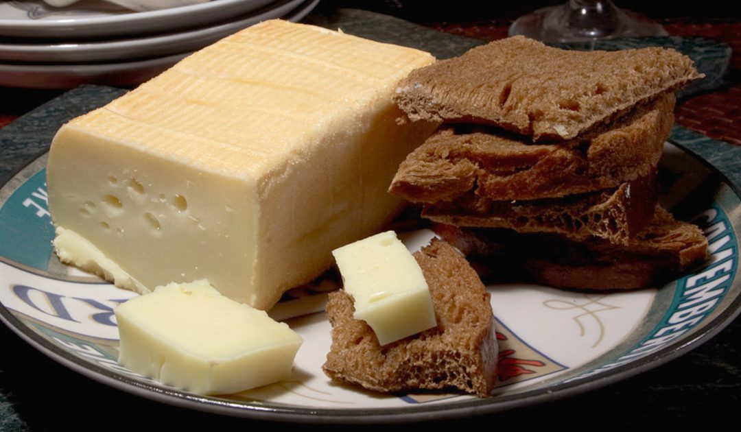 A block of Limburger Cheese on a plate with cheese slices and dark rye bread